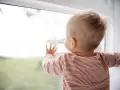 Małe dziecko w paski patrzy przez okno, dotykając szyby.