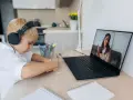 Chłopiec w słuchawkach uczy się zdalnie, patrząc na ekran laptopa z nauczycielem.