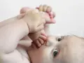 Niemowlę wkłada stópkę do buzi, patrząc w górę.