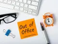 Biurko z klawiaturą, okularami, karteczką "Out of Office", zegarkiem i długopisem.