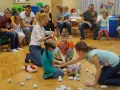 Zajęcia integracyjne z rodzicami w przedszkolu: dzieci z zawiązanymi oczami szukają prezentu, rodzice obserwują.