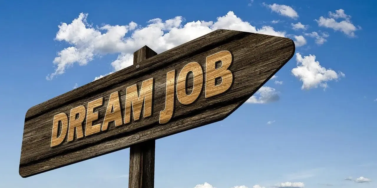Drewniany drogowskaz z napisem "DREAM JOB" na tle błękitnego nieba z chmurami.