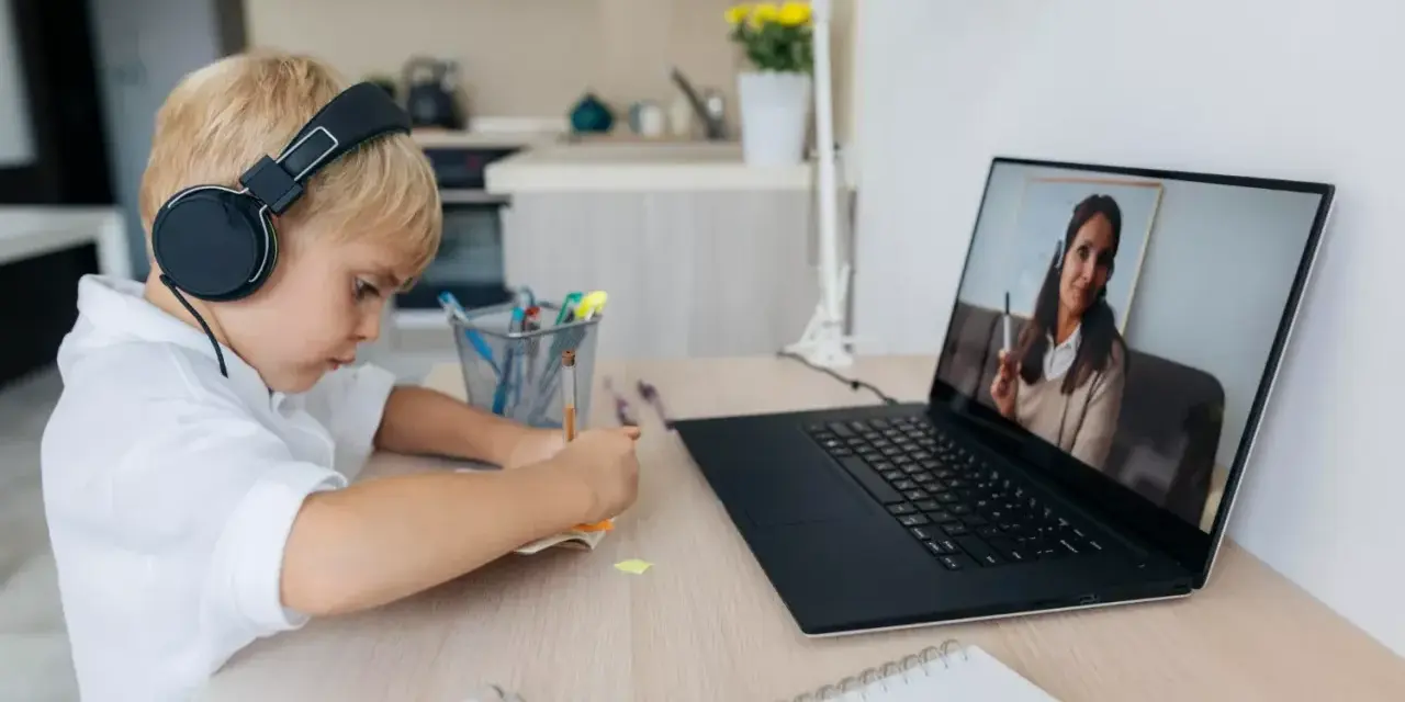 Chłopiec w słuchawkach uczy się zdalnie, patrząc na ekran laptopa z nauczycielem.