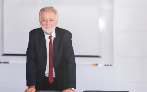 Uśmiechnięty starszy mężczyzna w garniturze stoi przy stole w sali konferencyjnej.