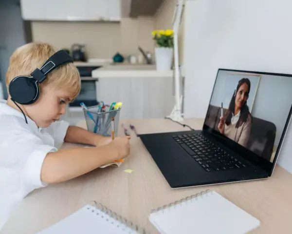 Chłopiec w słuchawkach uczy się zdalnie, patrząc na ekran laptopa z nauczycielem.