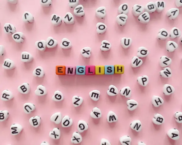 Kolorowe koraliki z literami tworzą napis "ENGLISH" na różowym tle.