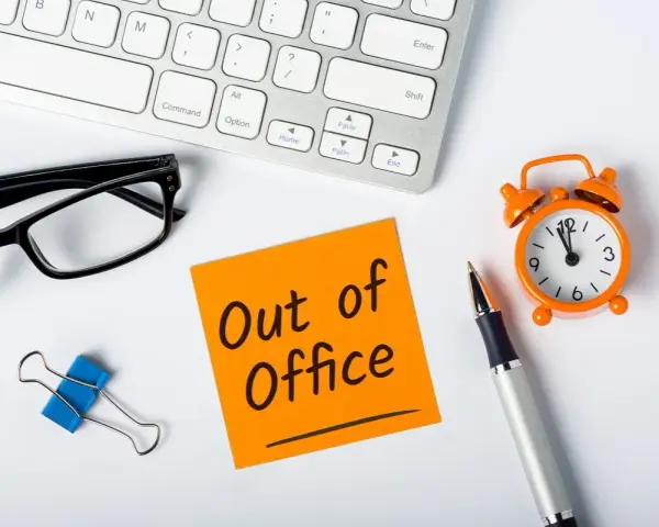 Biurko z klawiaturą, okularami, karteczką "Out of Office", zegarkiem i długopisem.