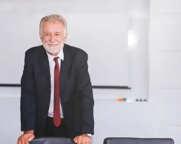 Uśmiechnięty starszy mężczyzna w garniturze stoi przy stole w sali konferencyjnej.